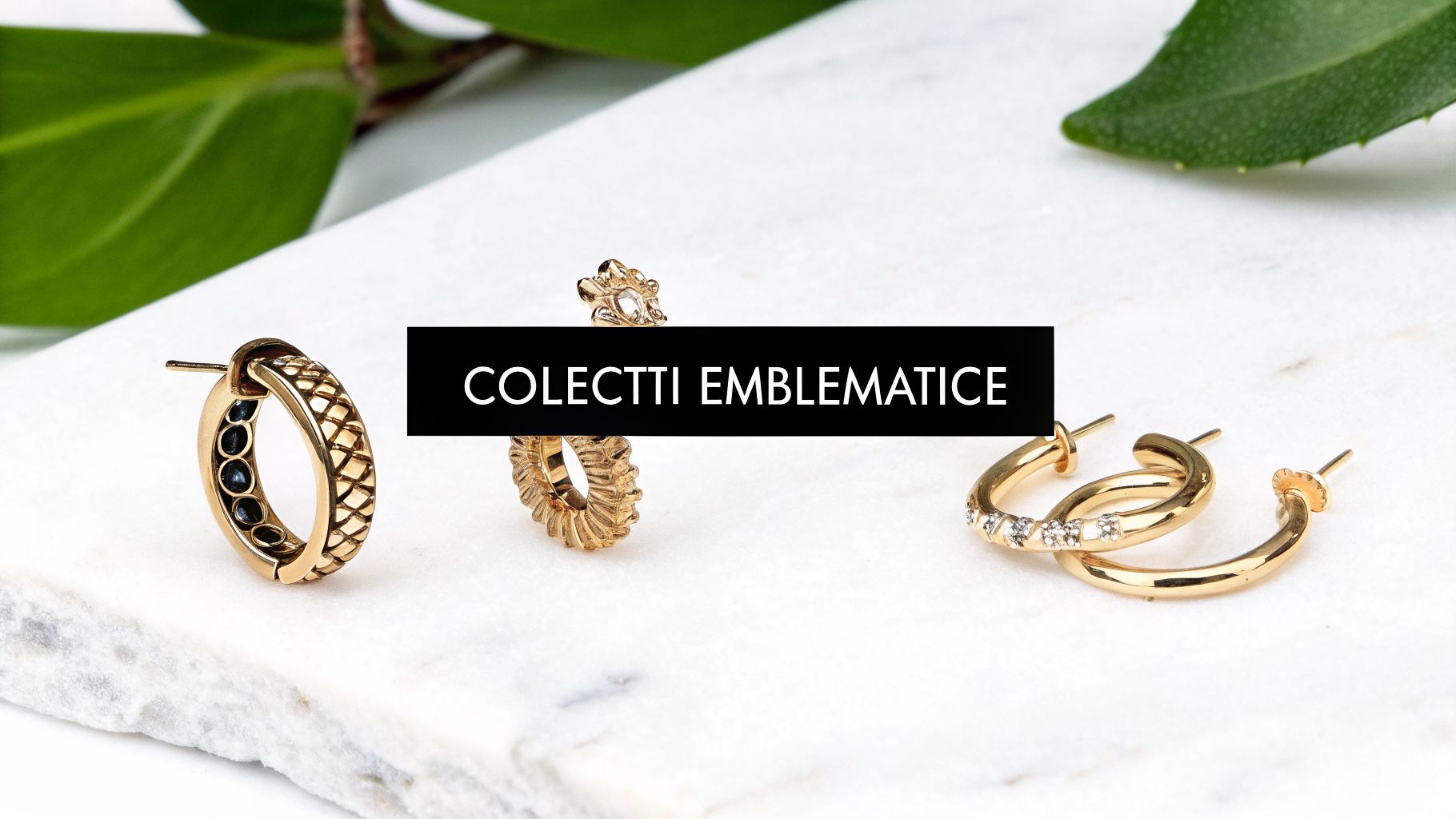 Cercei aurii variați, unii cu pietre negre și alții cu pietre albe, pe marmură albă, evidențiind colecția emblematică.